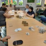 Fotografija prikazuje uporabnike v kooperacijski delavnici med opravljanjem dela- pakiranje vijakov.